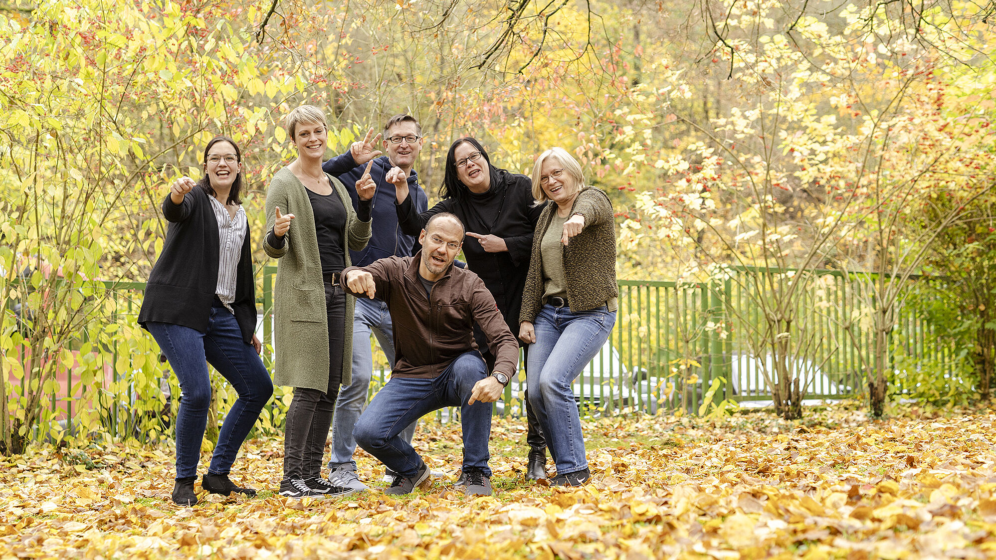 Eine lachende Gruppe die mit den Fingern aufeinander, in die Kamera und in die Luft zeigen.