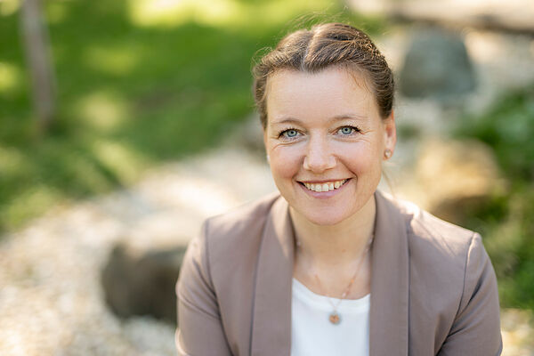 Foto einer lächelnden Frau im mittleren Alter mit hellbraunen Haaren in einem Zopf.